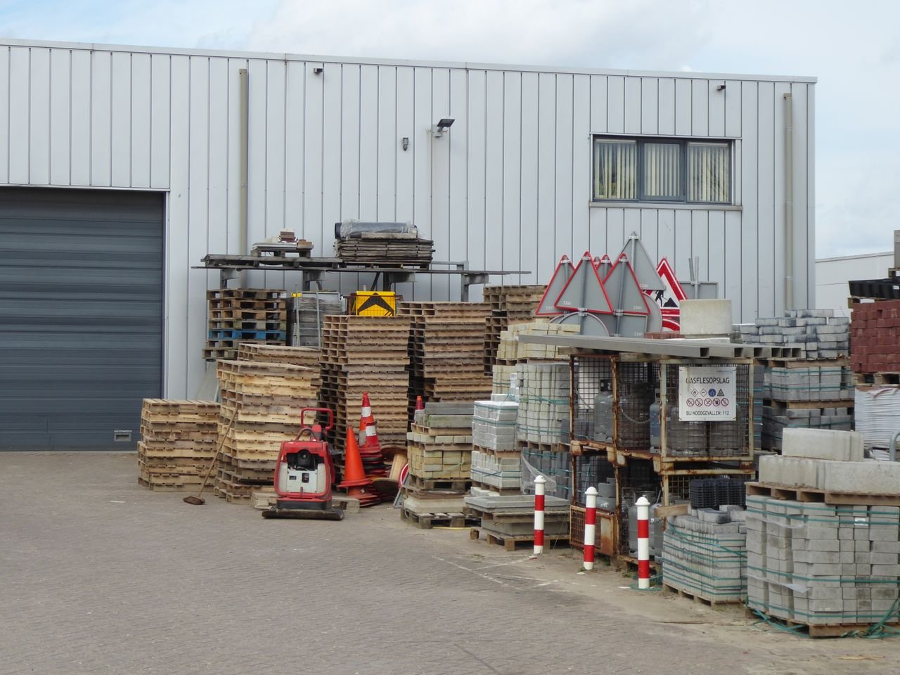 An outdoor yard with stacked construction supplies and pallets against a warehouse.